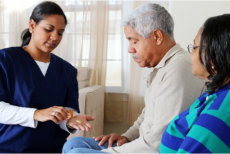 caregiver giving elderly man his medicine with his wife at his side